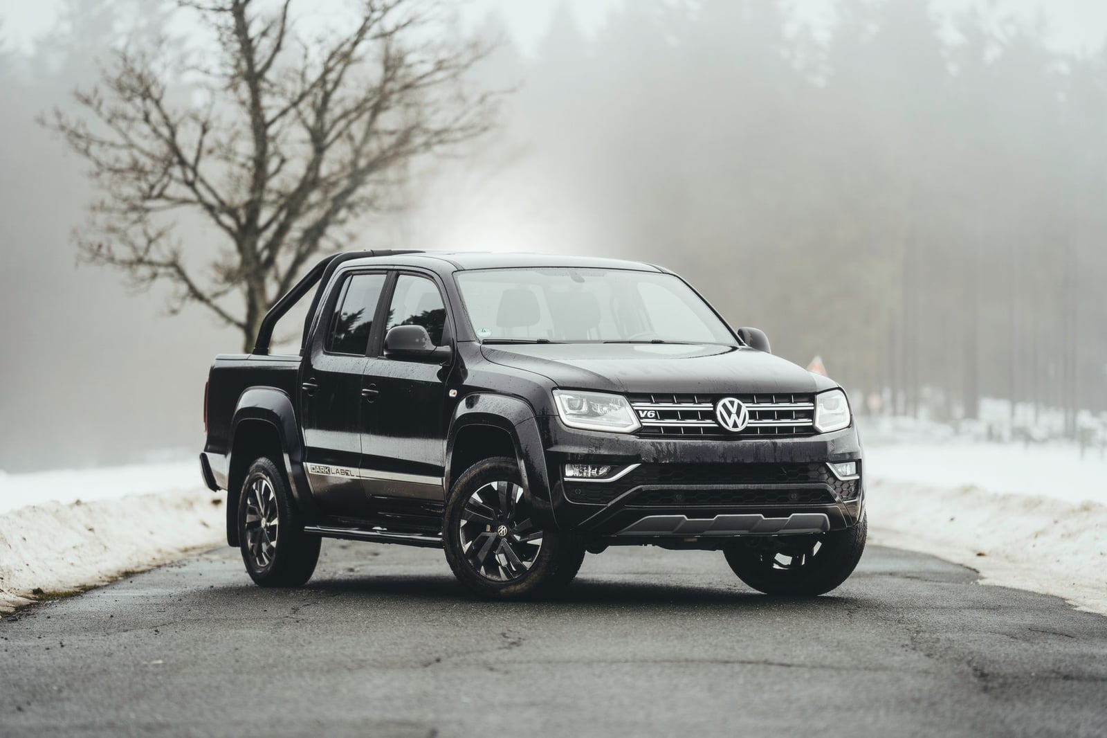 Camioneta negra de Volkswagen en un camino rural nevado con árboles invernales envueltos en niebla.
