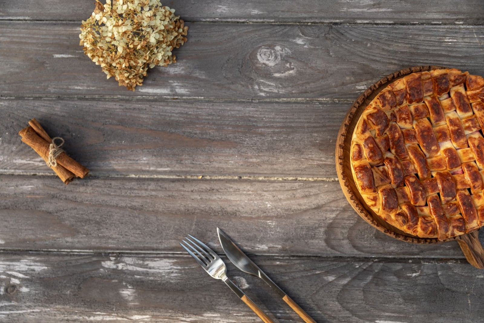 Vista superior de una tarta de manzana rústica en una mesa de madera con palitos de canela, cuchillo y tenedor.