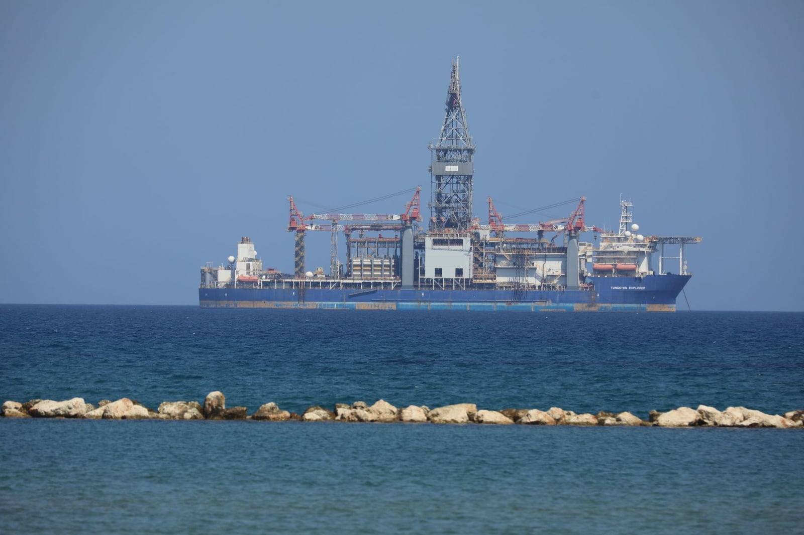 Una plataforma petrolera offshore flota en un mar tranquilo con un cielo azul claro de fondo.