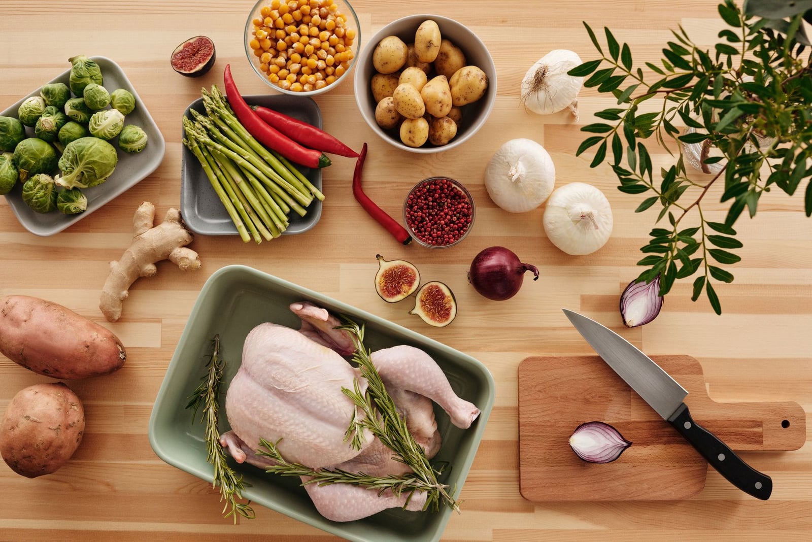 Vista superior de ingredientes frescos para cocinar sobre una superficie de madera, con pollo, verduras y hierbas.