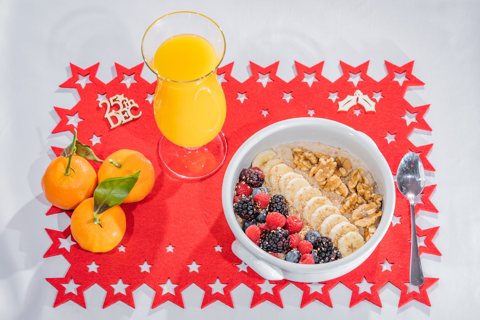 Un desayuno vibrante con frutas, nueces y jugo sobre un tapete con temática navideña.