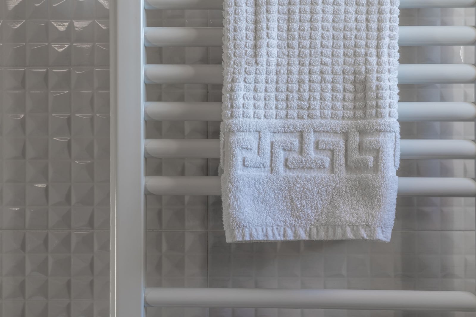Toalla blanca sobre un radiador en un baño moderno y minimalista con paredes de azulejos.