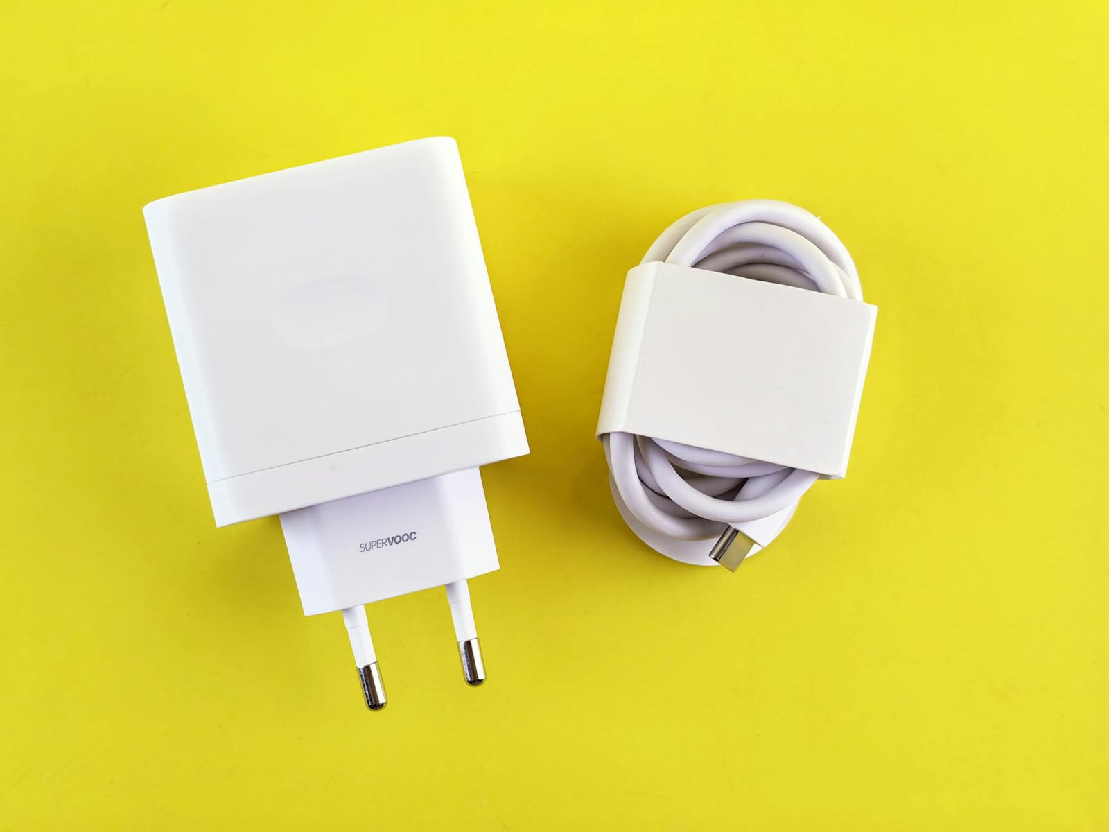 Cargador y cable SuperVOOC de color blanco sobre un fondo amarillo brillante, que muestra un diseño minimalista.
