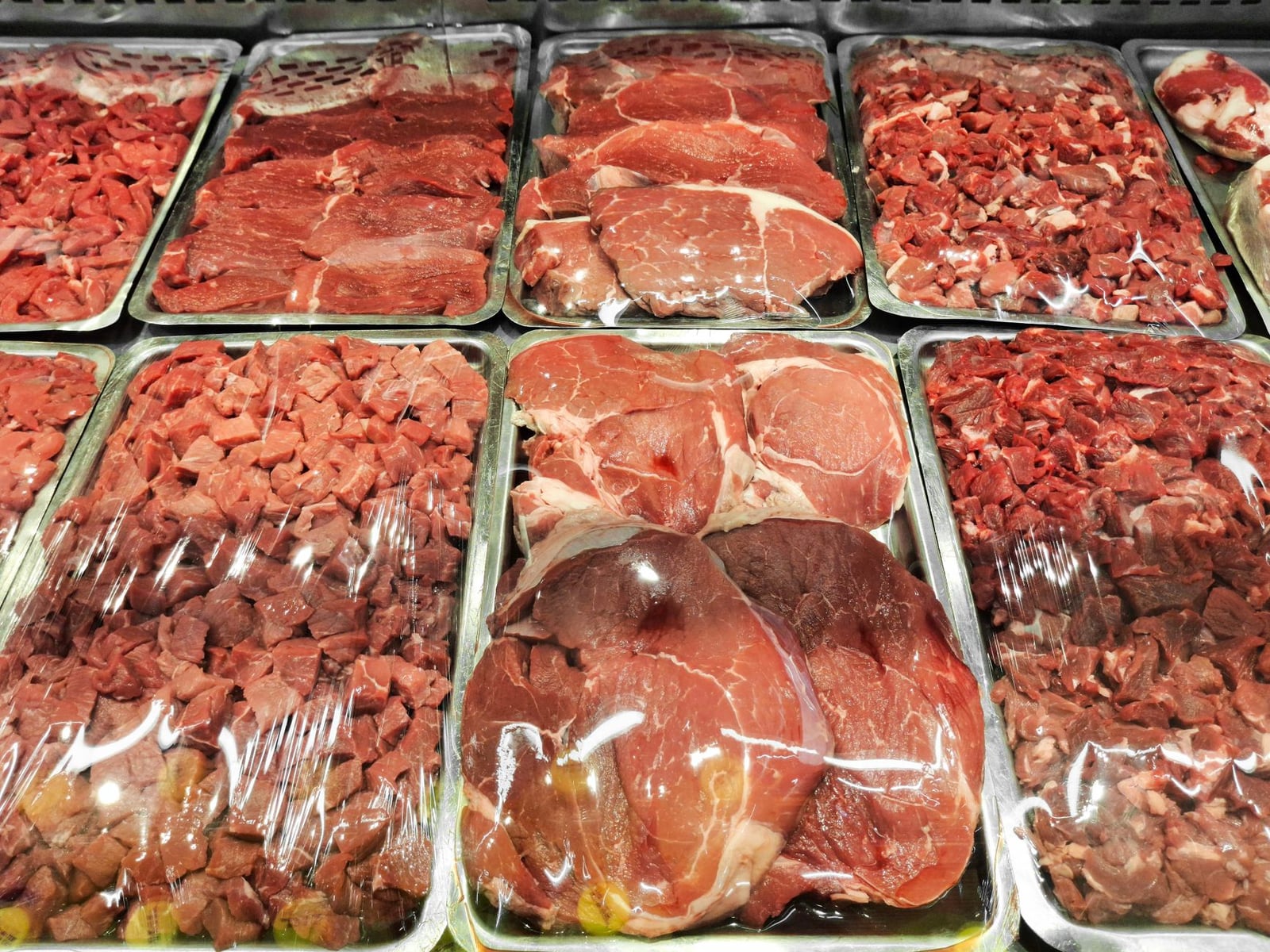 Diversos cortes de carne cruda expuestos ordenadamente en la sección refrigerada de un supermercado.