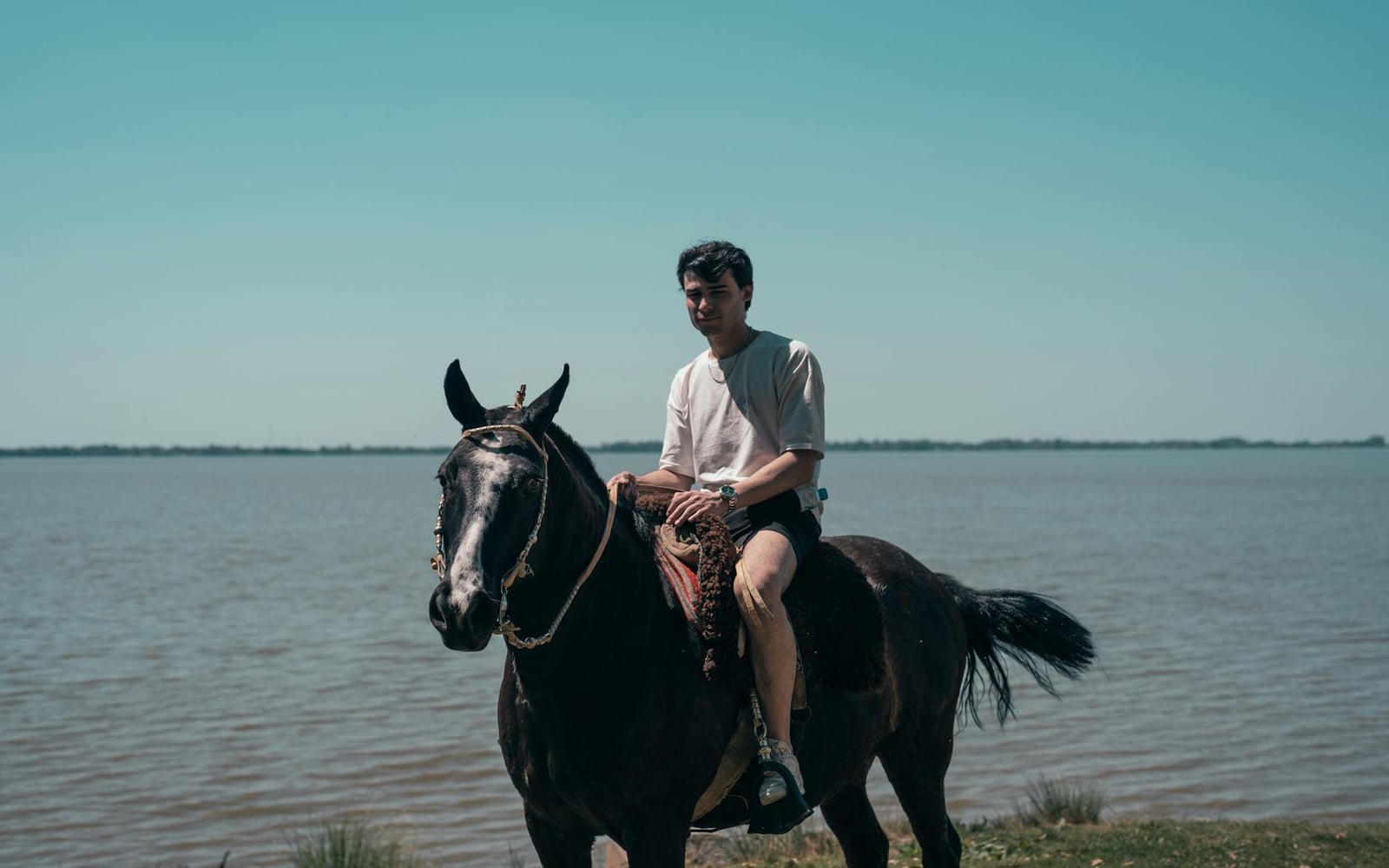 Una persona montando a caballo cerca de un lago en un día soleado en Chascomús, Argentina.