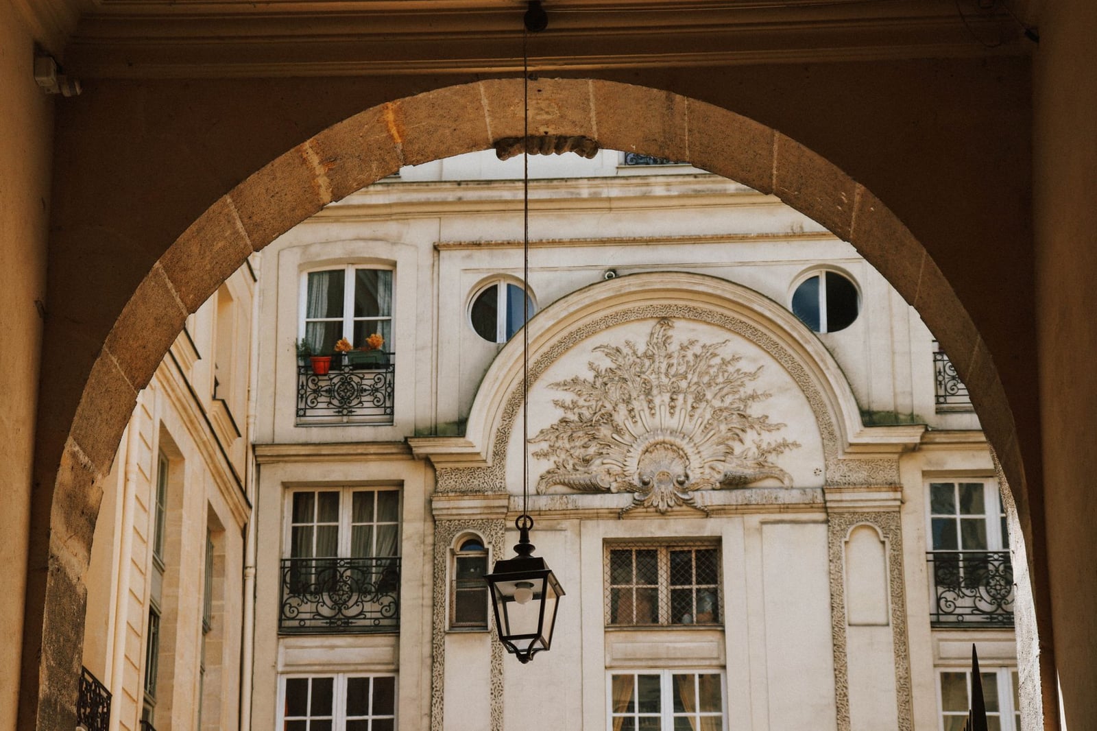 Vista de la fachada decorada de un edificio parisino enmarcada por un arco con una linterna decorativa.