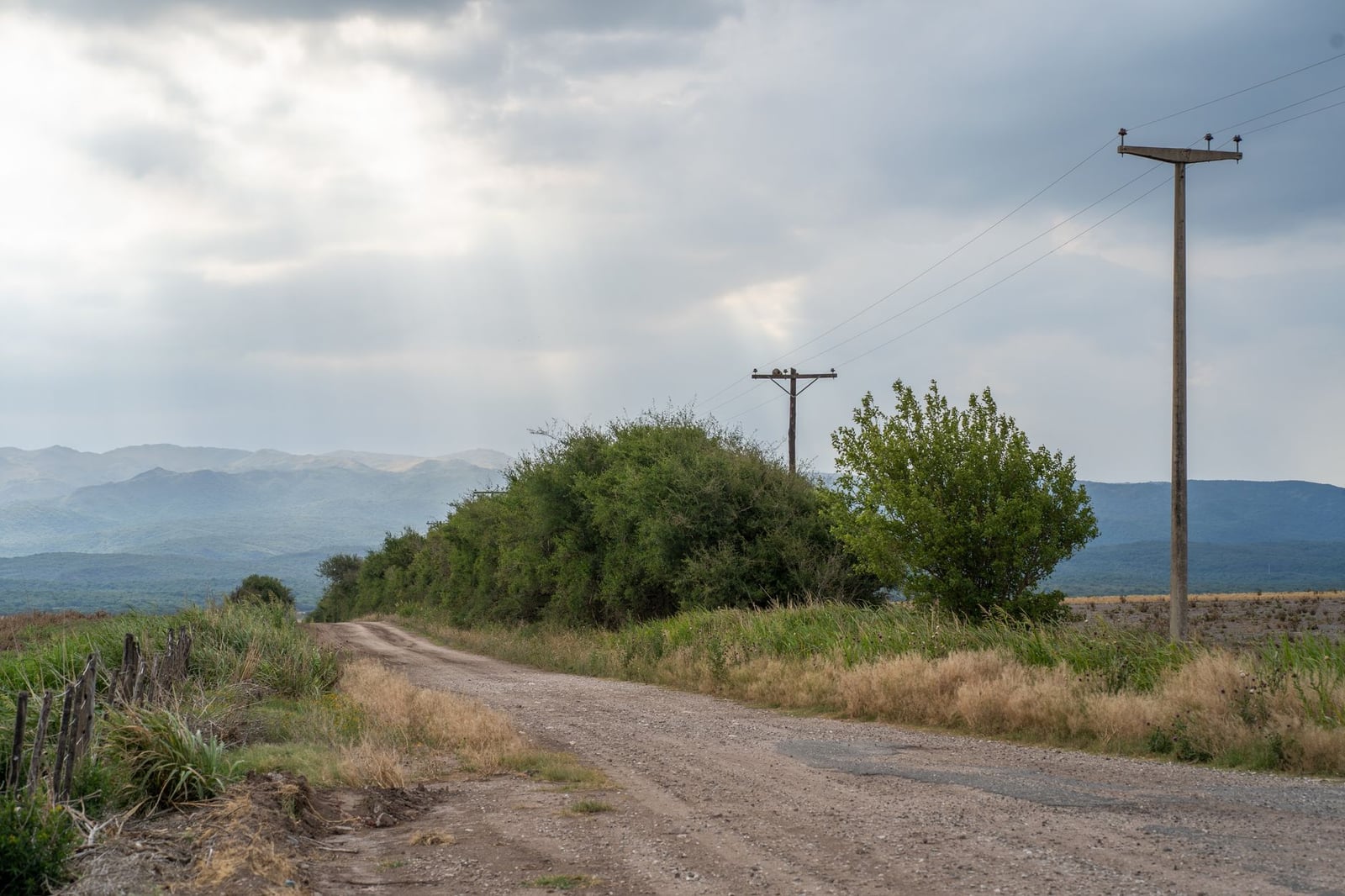 Una tranquila escena rural con un camino de tierra, líneas eléctricas y un paisaje montañoso de fondo en Córdoba, Argentina.
