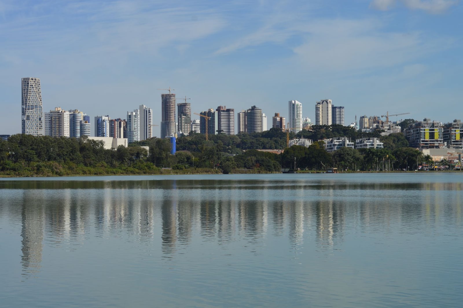 Horizonte de Curitiba, Brasil, reflejado en un lago sereno bajo un cielo azul despejado.
