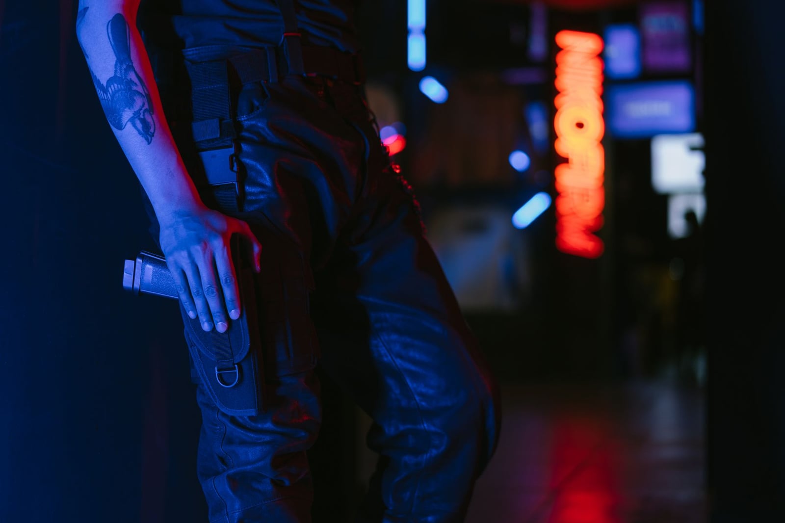 Una persona con pantalones de cuero sosteniendo un arma en un entorno iluminado por neón.