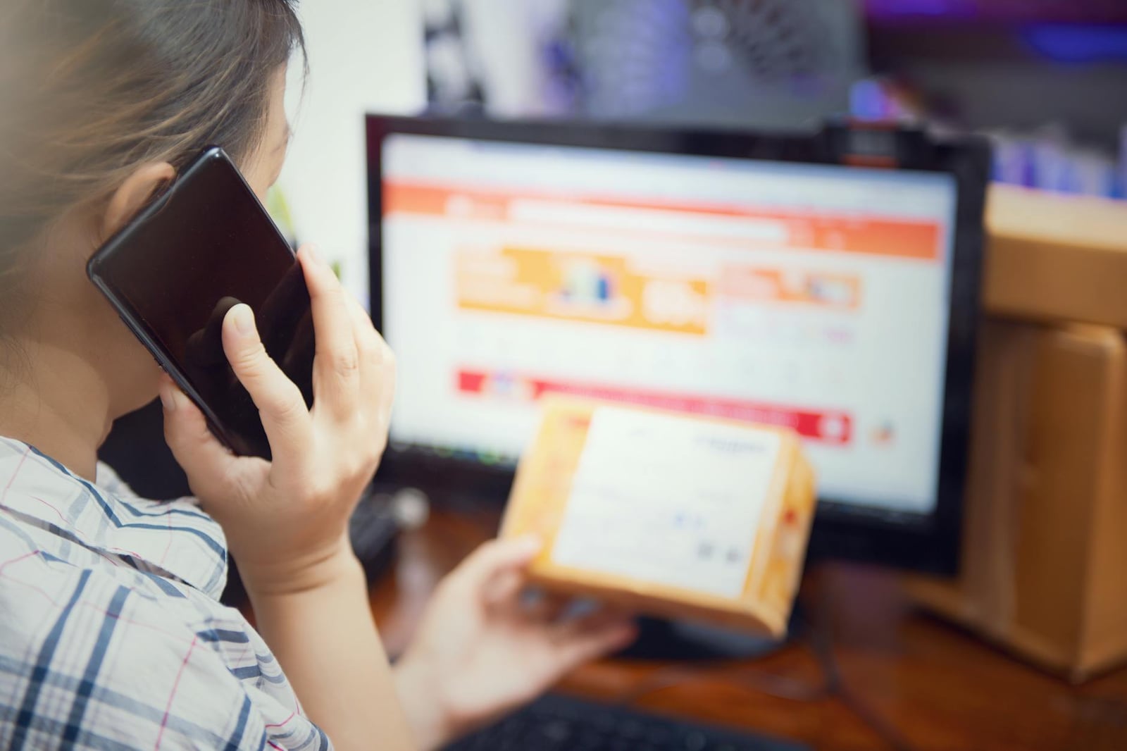 Mujer realizando múltiples tareas al utilizar un teléfono y revisar un paquete de compra en línea en casa.