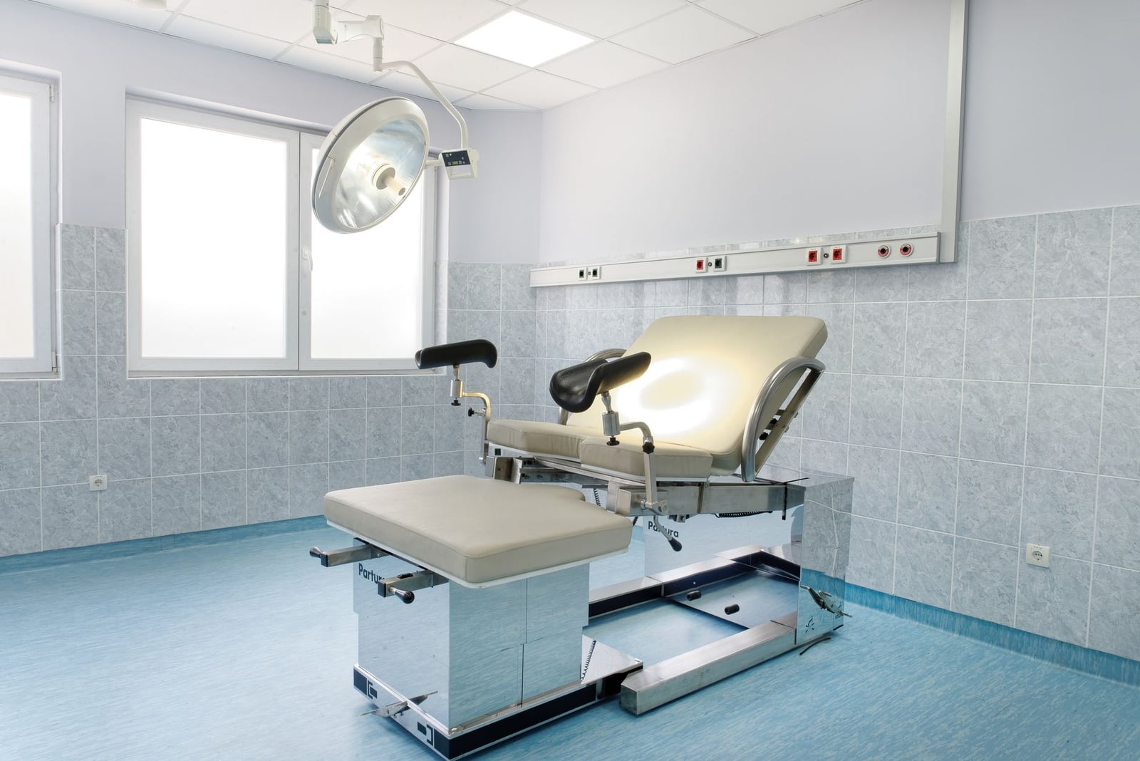 Sala de exploración ginecológica luminosa con sillón regulable y luz de techo en un centro médico.