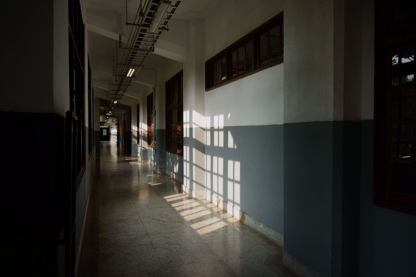 La luz del sol proyecta sombras en un pasillo vacío de un edificio moderno, creando una atmósfera serena y contemplativa.