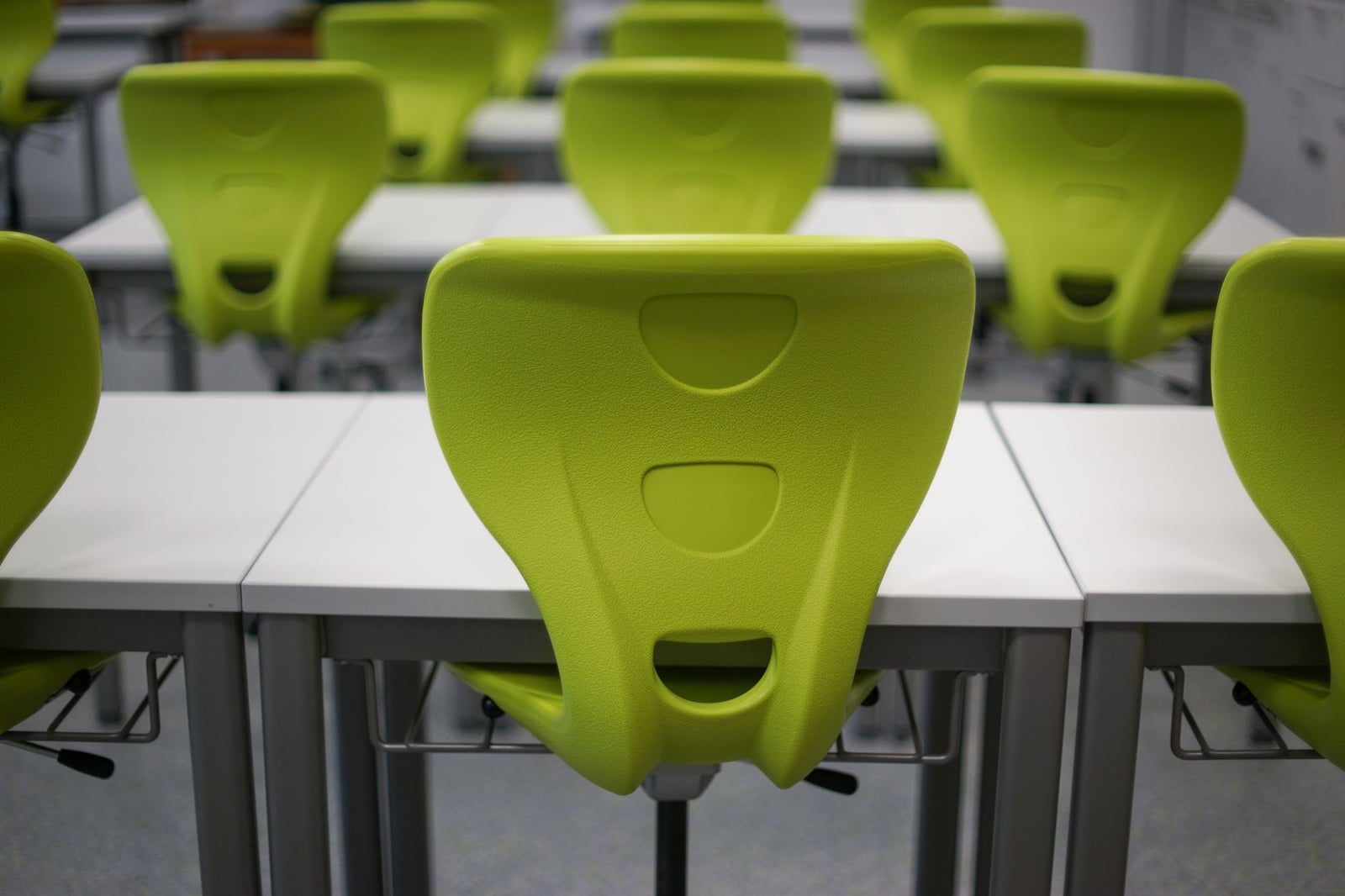 Un aula moderna vacía con filas de sillas de plástico verde vibrante y mesas blancas.
