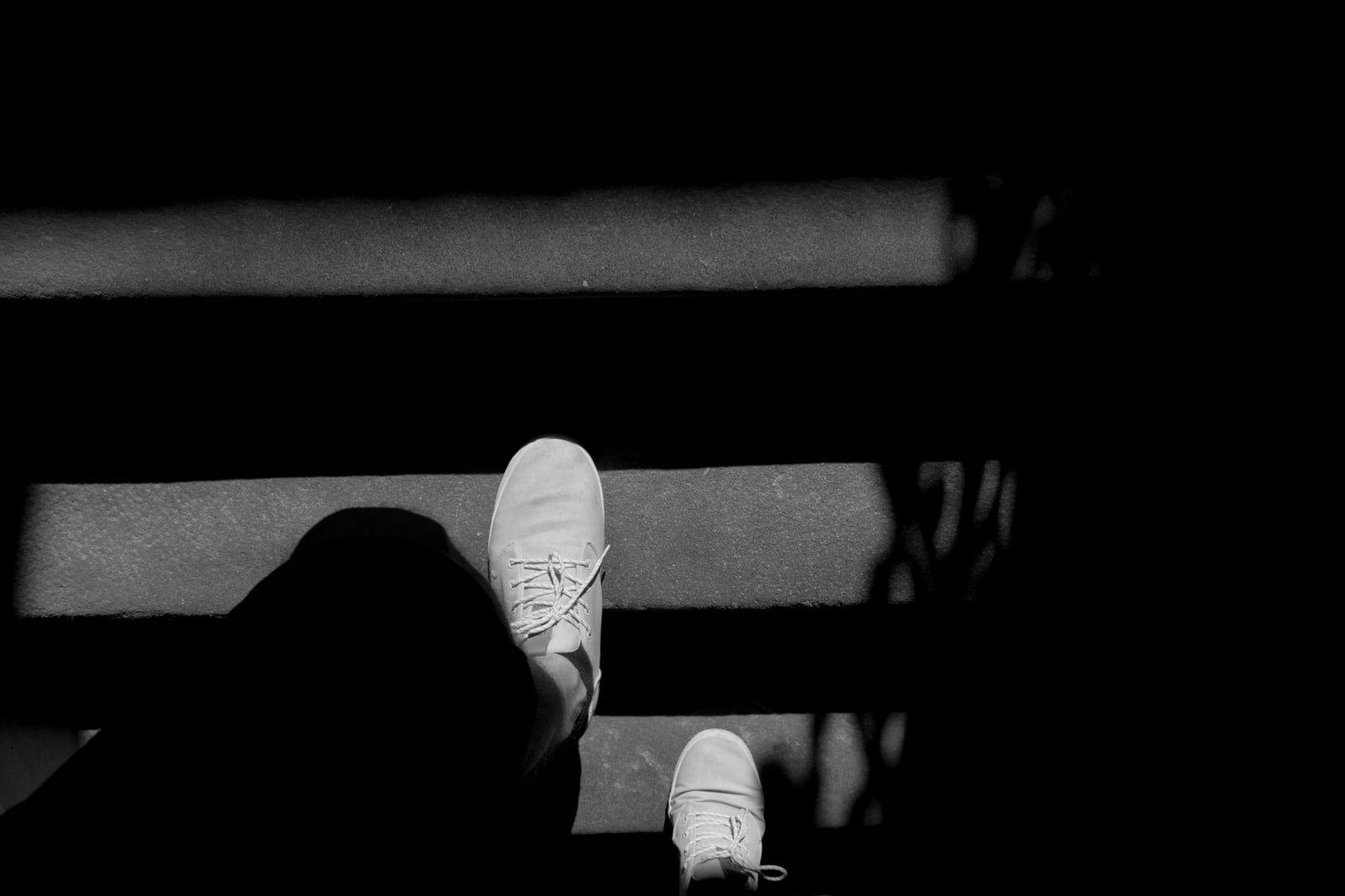 Imagen monocromática de alto contraste de zapatillas bajando escaleras de concreto con sombras dramáticas.