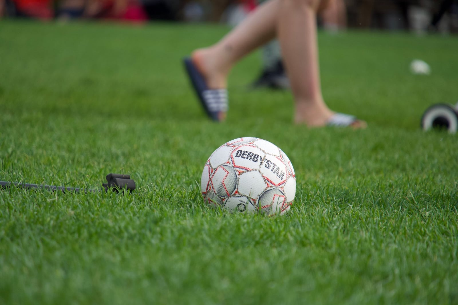 Primer plano de un balón de fútbol en un campo verde, con jugadores borrosos al fondo.