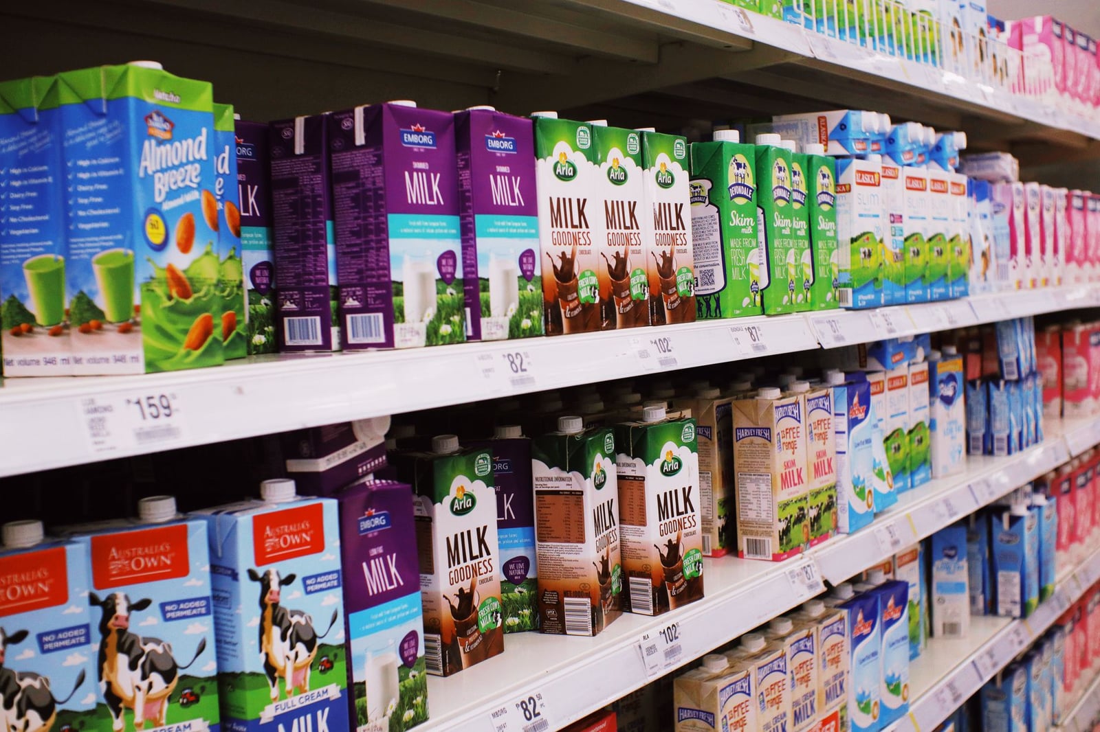 Varios cartones de leche exhibidos en estantes en un pasillo brillante de supermercado.