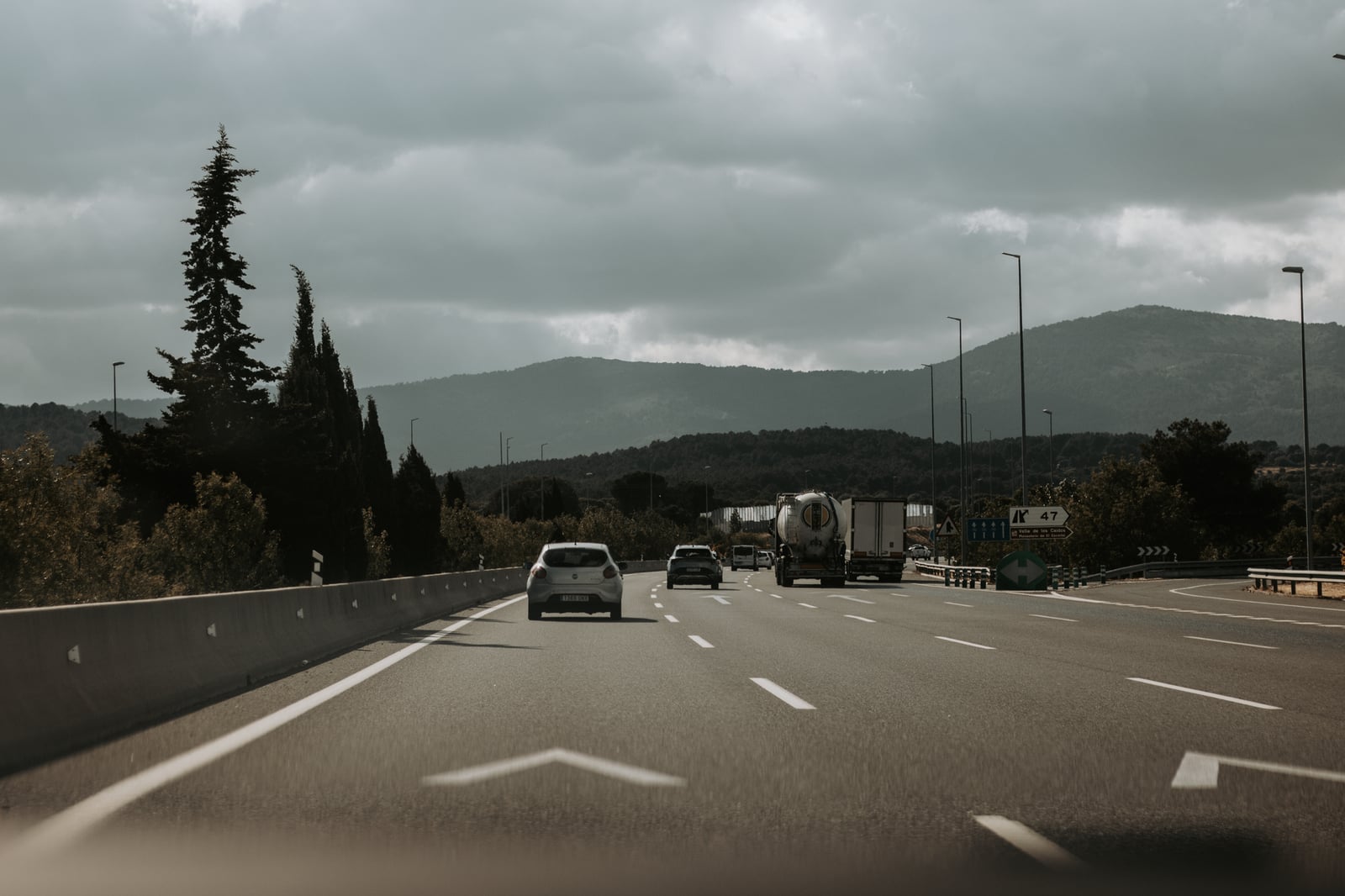 Coches circulan por una autopista a través de un paisaje montañoso escénico bajo cielos nublados.