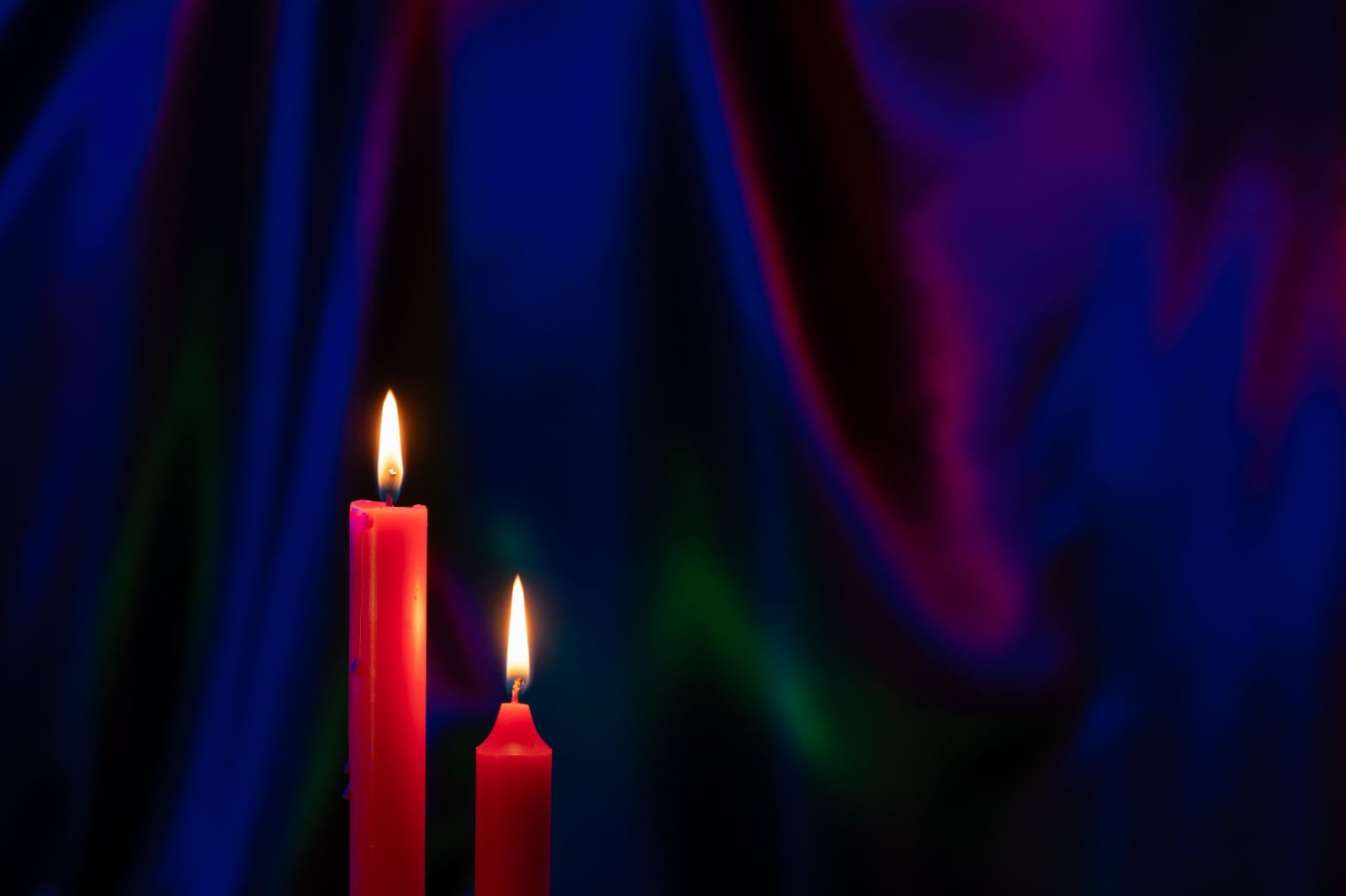 Dos velas rojas con llamas vibrantes sobre un fondo de cortinas ricas y coloridas, creando una atmósfera cálida y acogedora.