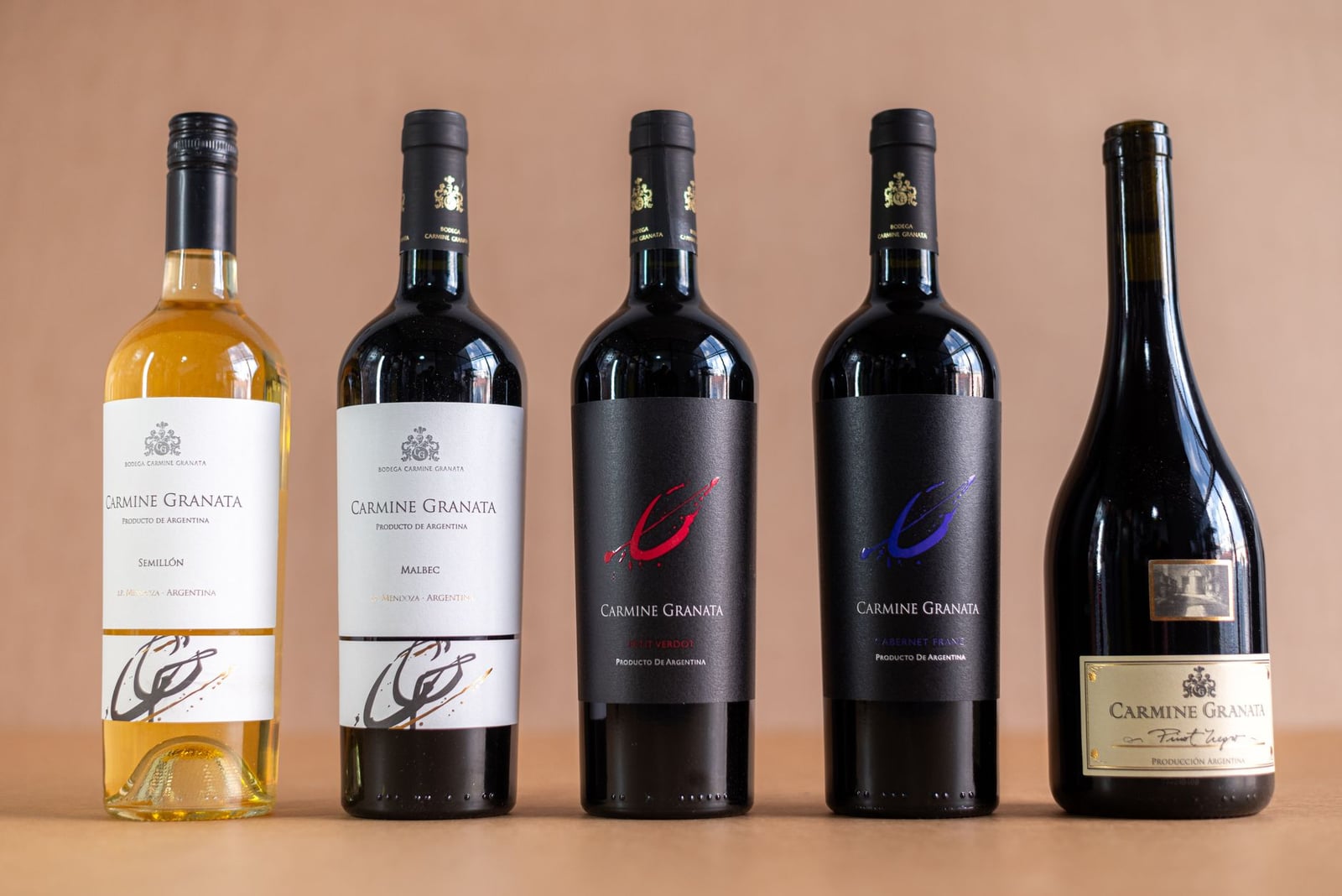 Fotografía de estudio de botellas de vino Carmine Granata que muestran varios tipos, sobre un fondo liso.