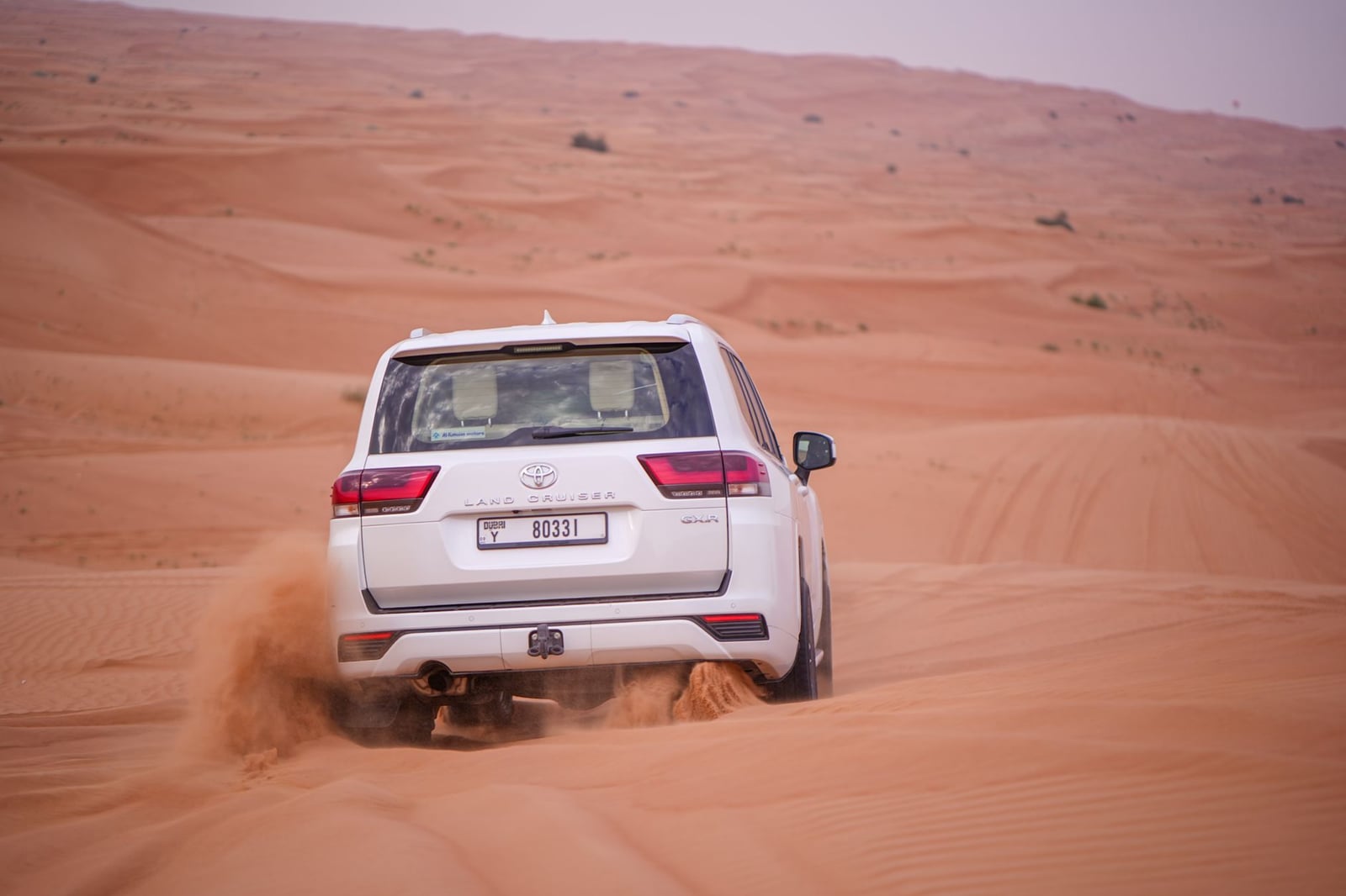 Un Toyota Land Cruiser conduce activamente a través de un vasto desierto, mostrando sus capacidades todoterreno.