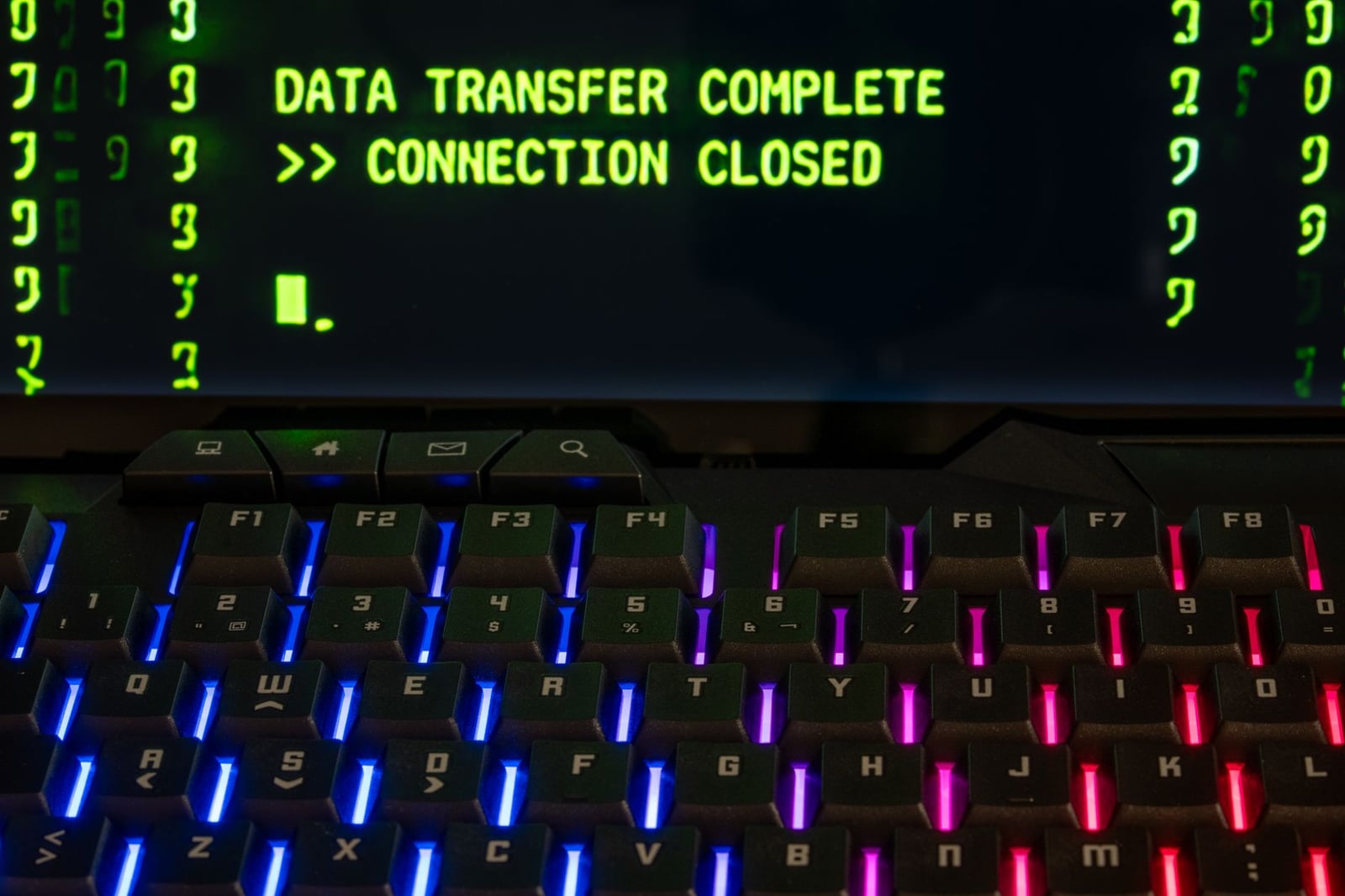 Primer plano de un teclado iluminado por RGB con una pantalla que muestra 'Transferencia de Datos Completa'.