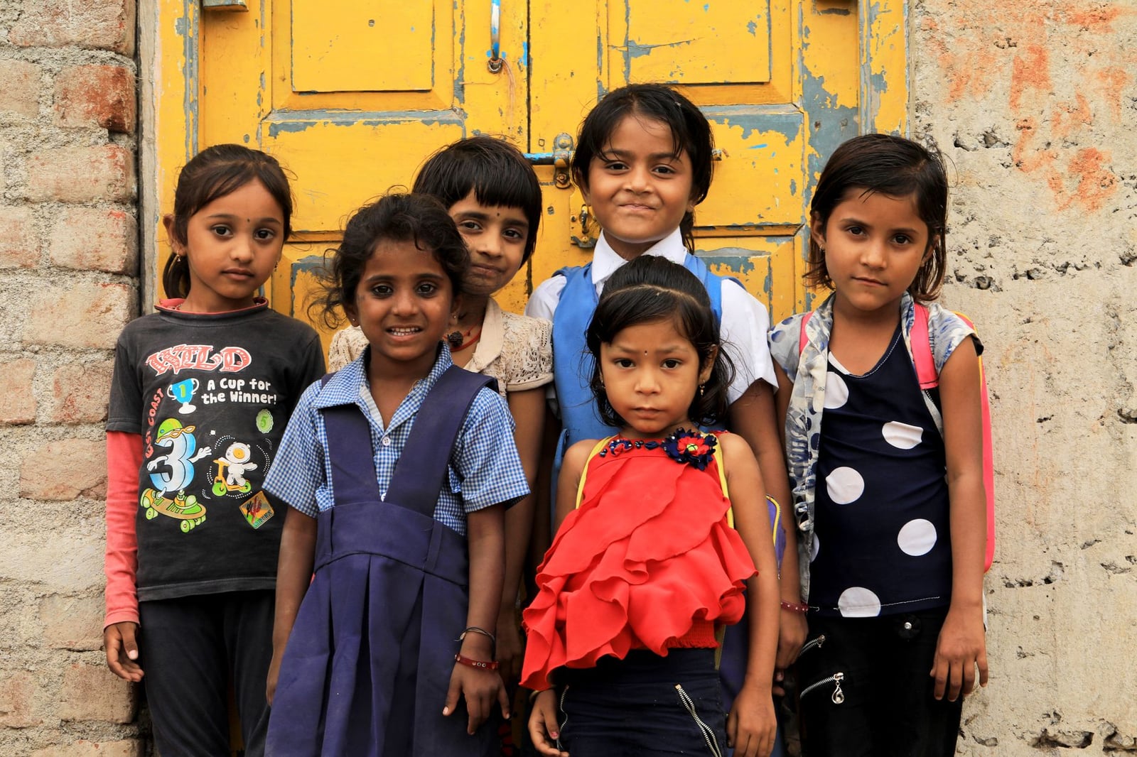 Un grupo de seis niños del sur de Asia sonriendo y posando juntos frente a una puerta antigua y colorida.