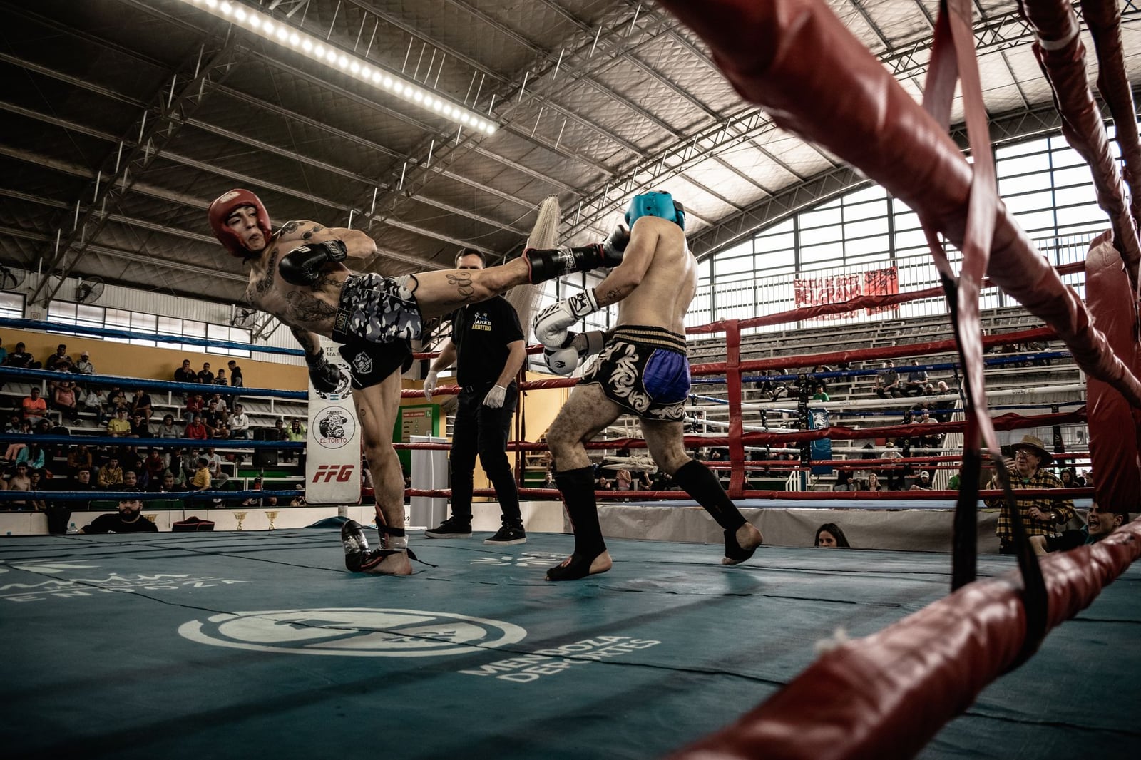 Captura de acción intensa de un combate de kickboxing en una arena llena, mostrando atletismo y habilidad.
