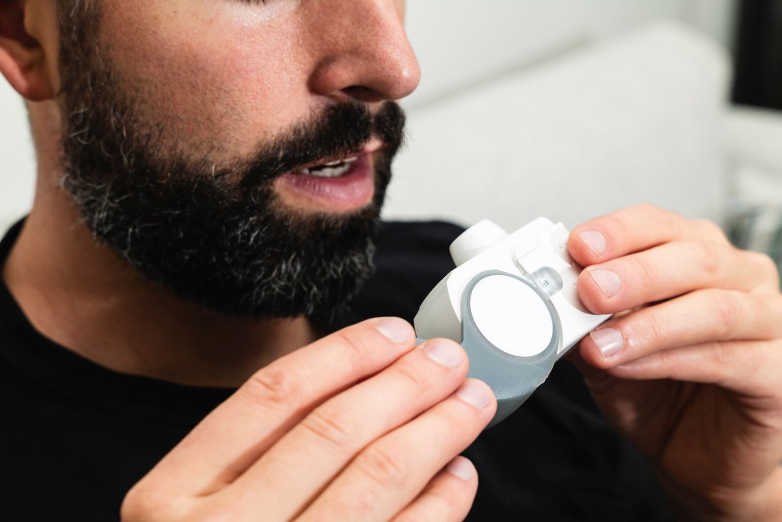 Primer plano de un hombre barbudo sosteniendo un inhalador, lo que indica atención respiratoria.