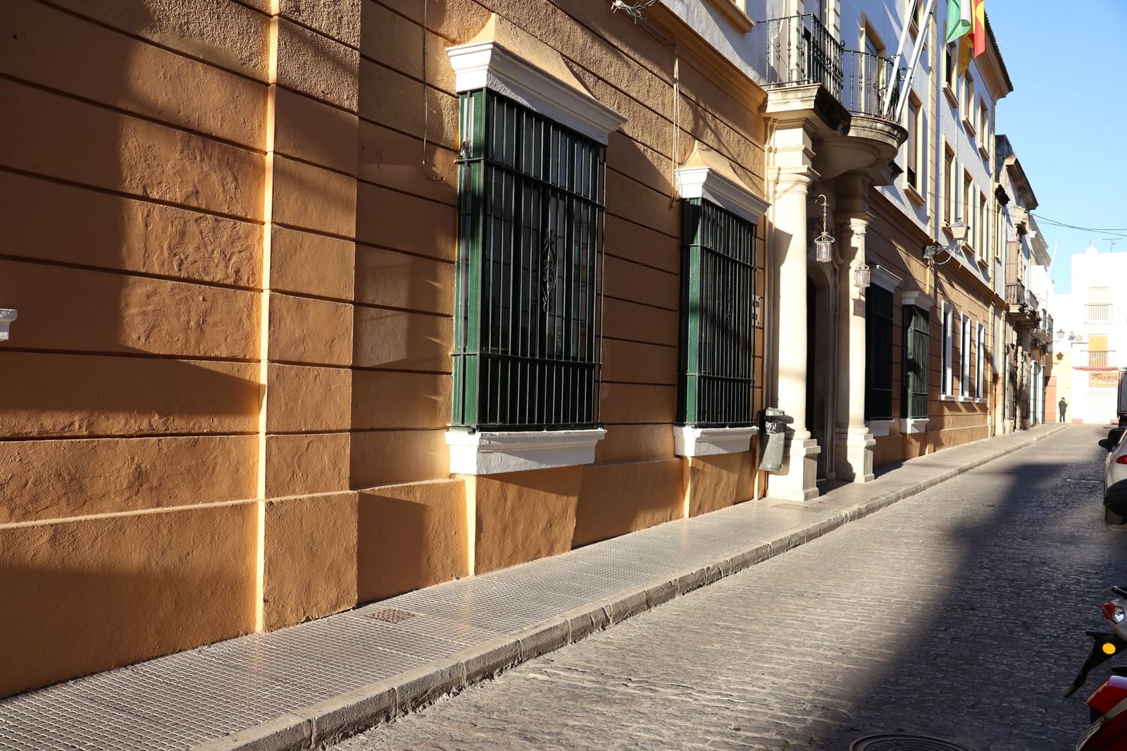 Fachada iluminada por el sol de un edificio histórico en una calle estrecha en El Puerto de Santa María, España.