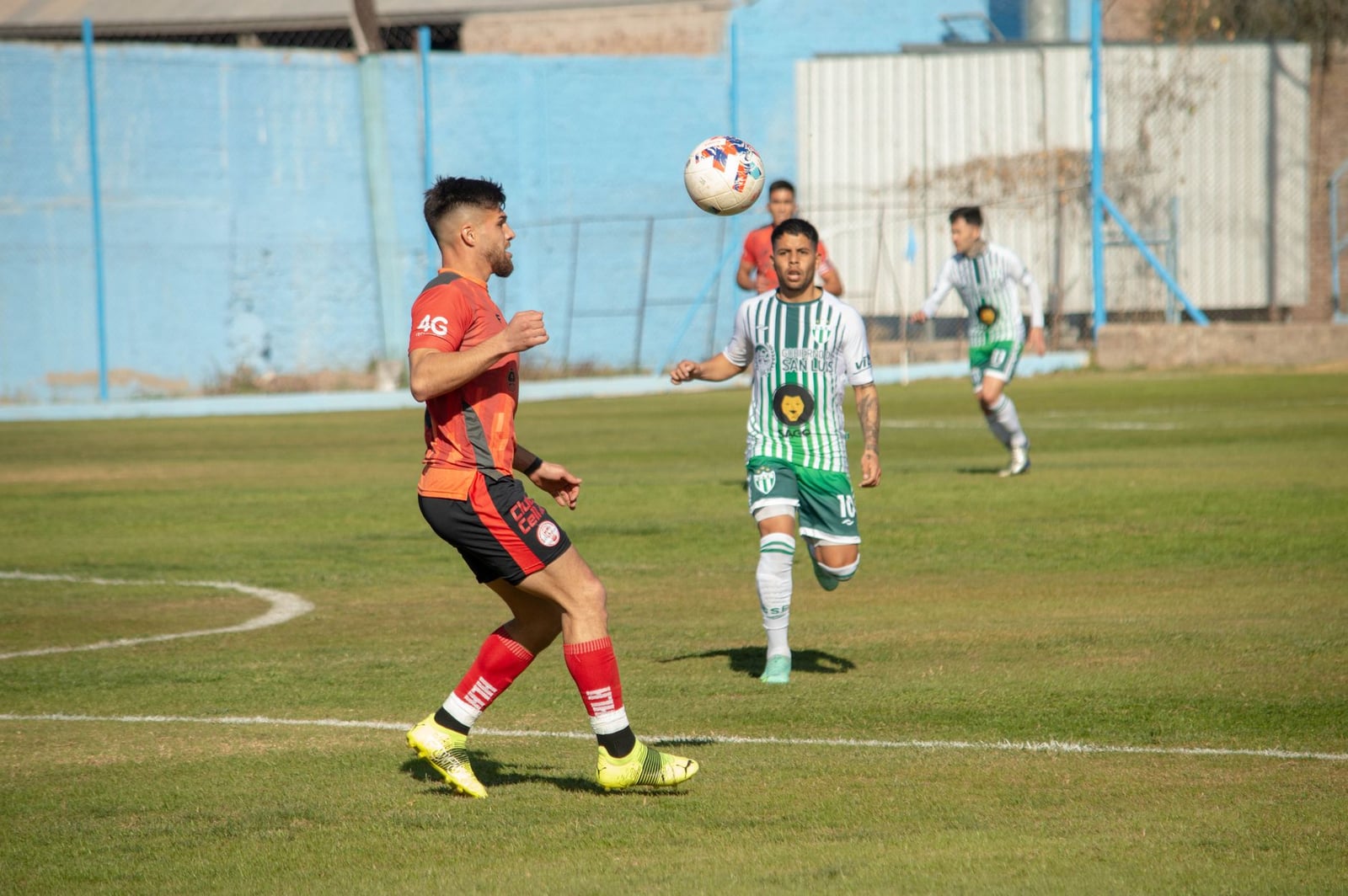 Acción intensa de fútbol en Mendoza, Argentina, con jugadores en movimiento en un día soleado.