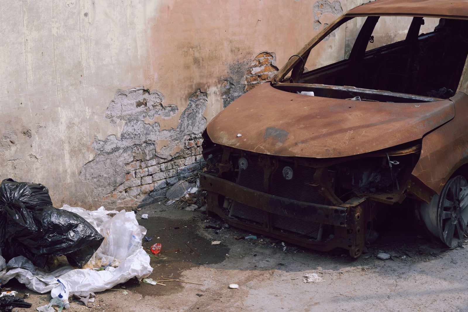 Un coche oxidado y basura en un entorno urbano abandonado, que simbolizan la decadencia de la ciudad.