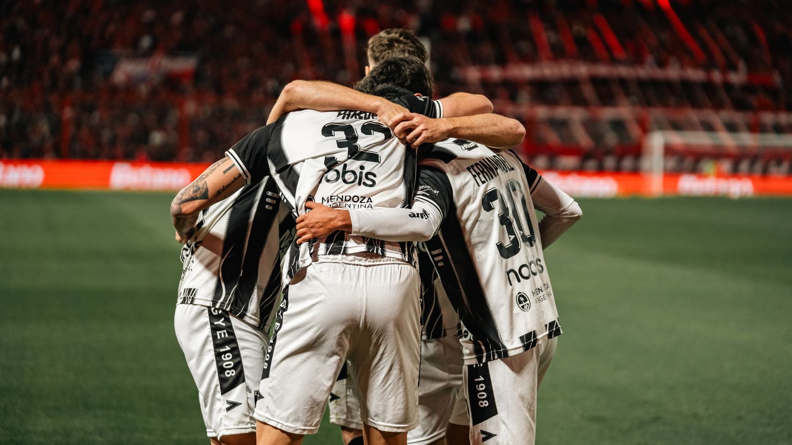 Jugadores de fútbol con camisetas blancas y negras celebrando una victoria con un abrazo grupal en el campo.