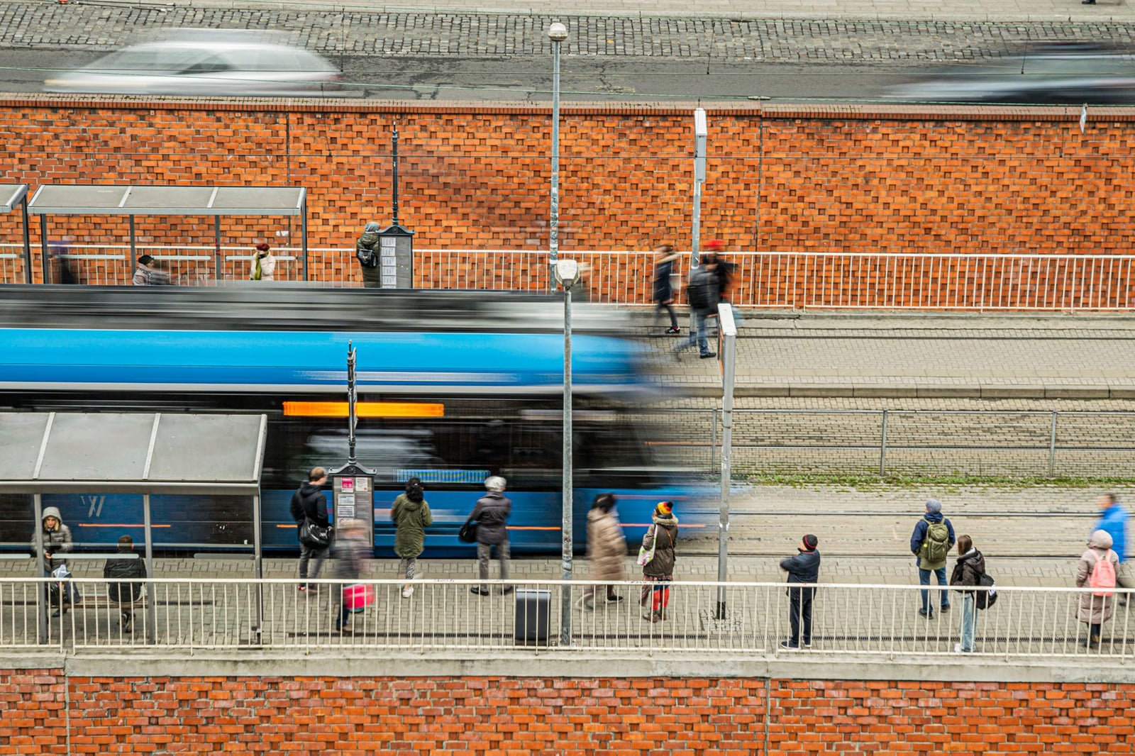 Personas esperando en una estación de tranvía, capturando la vida cotidiana urbana con desenfoque de movimiento.