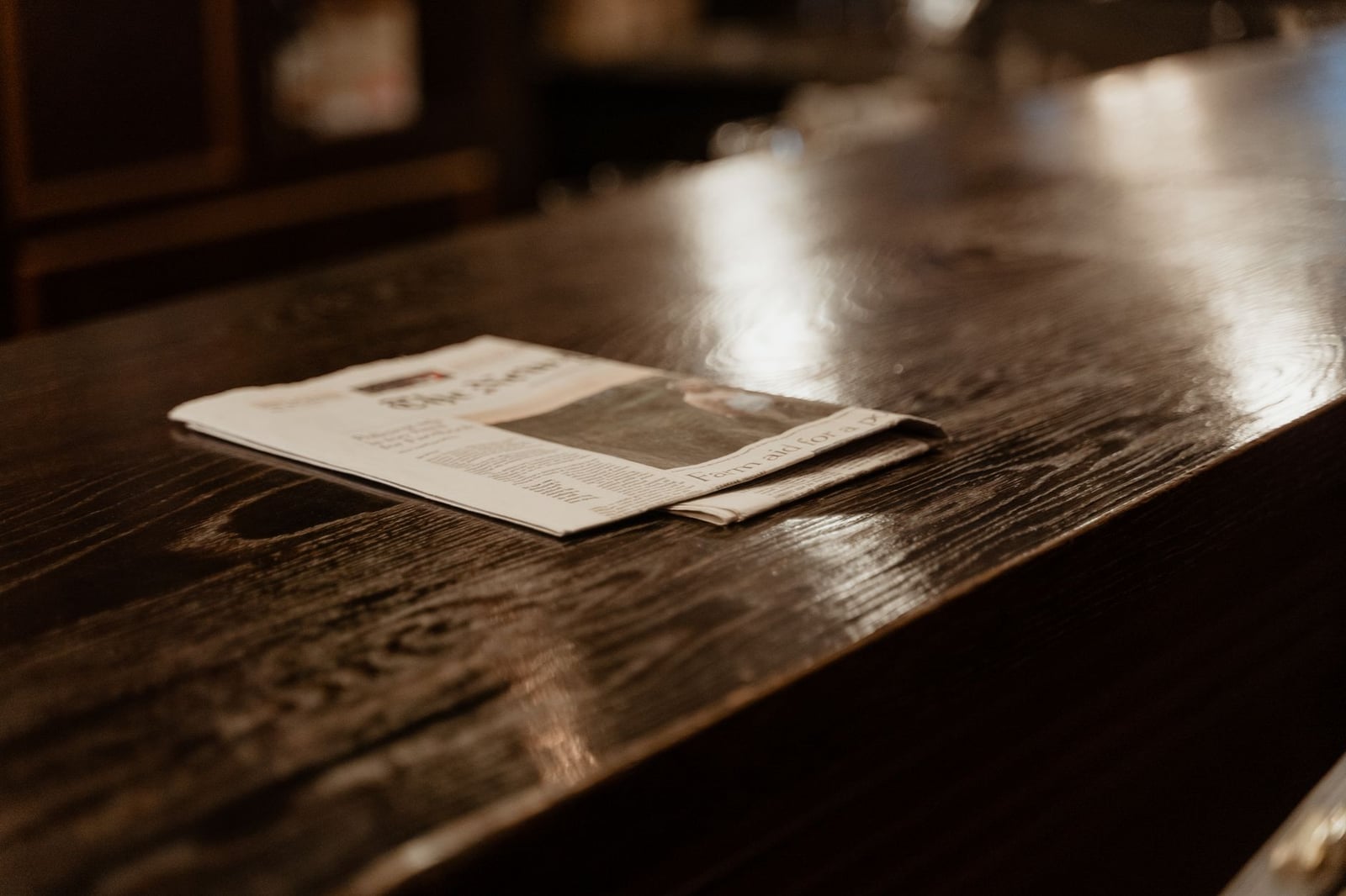 Una toma de still life de un periódico reposando sobre una mesa de madera pulida en un entorno interior acogedor.