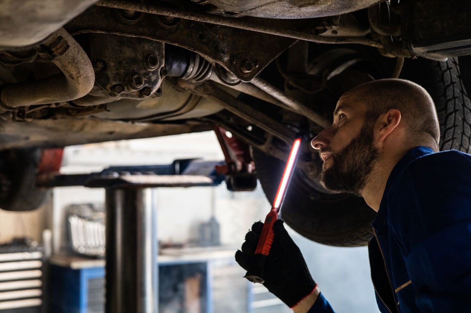 Mecánico usando luz para inspeccionar el chasis del vehículo en el taller para mantenimiento.
